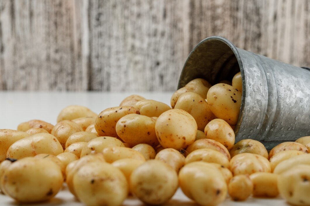 scattered-potatoes-from-mini-bucket-white-grungy-wooden-wall-side-vie